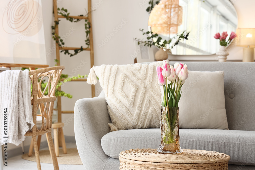 Fototapeta premium Vase with tulips on basket near sofa in living room