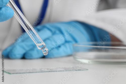 Female scientist dropping water sample onto glass on table in laboratory, closeup