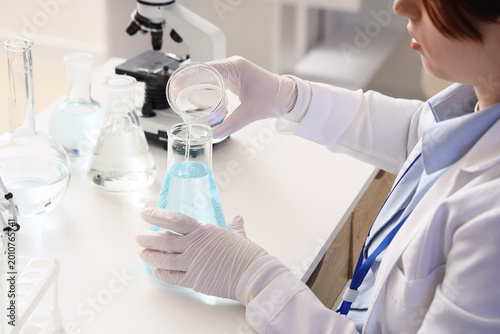 Female scientist pouring water sample into flask at table in laboratory, closeup