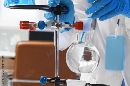 Female scientist dropping water sample into flask on stand in laboratory, clo...