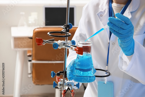 Female scientist dropping water sample into flask on stand in laboratory, clo...