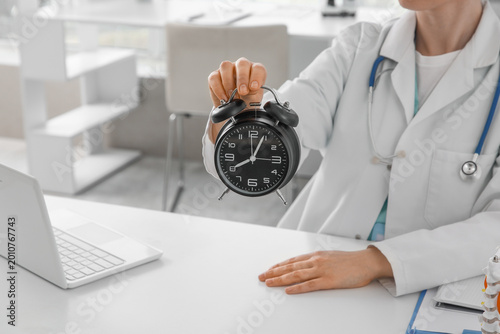 Female doctor with alarm clock at table in clinic