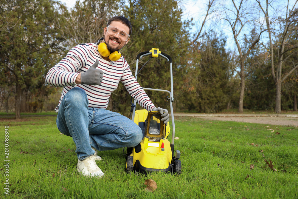 Fototapeta premium Young man with lawn mower showing thumb-up outdoors