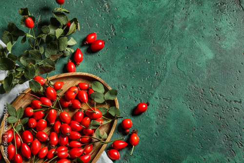 Foto Wooden plate with fresh rose hip berries and leaves on green background