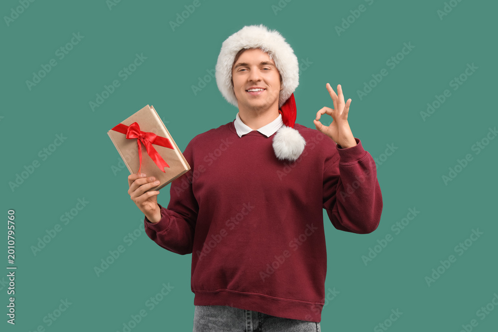 Fototapeta premium Young man in Santa hat and with book showing OK on green background
