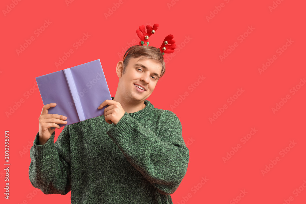 Fototapeta premium Young man with book on red background. Christmas celebration