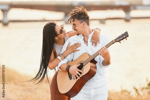 Foto Young couple of hippies with dreadlocks playing guitar at sunset