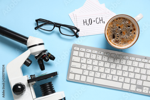 Modern microscope with keyboard, cup of coffee and eyeglasses on blue background