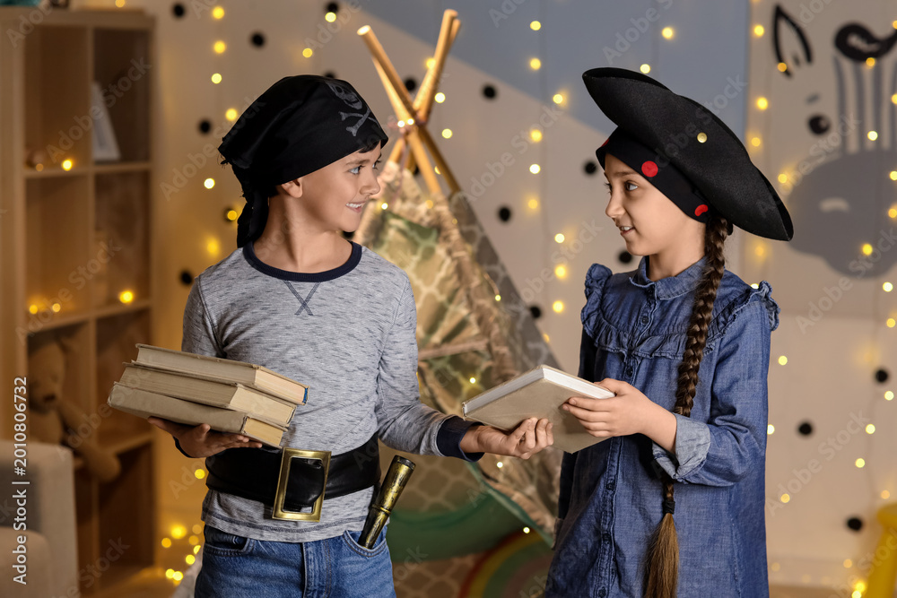 Fototapeta premium Cute children dressed as pirates with books at home in evening