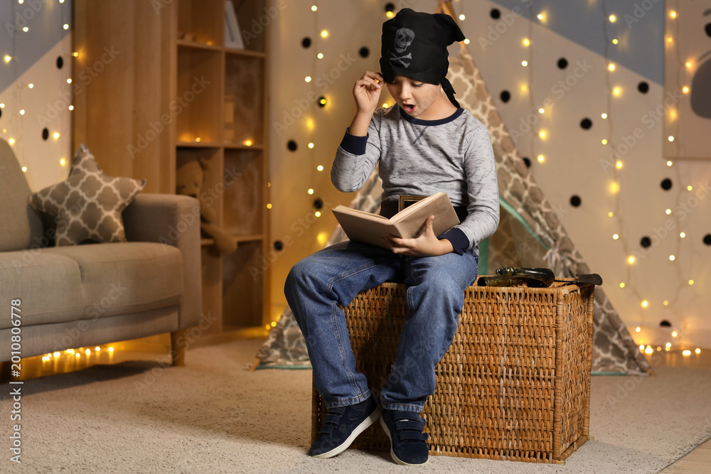 Fototapeta premium Shocked boy dressed as pirate reading adventure book at home in evening