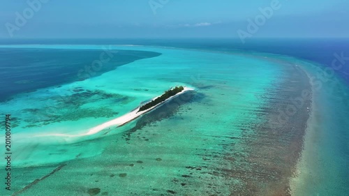 Aerial view of a narrow tropical island with lush green palm trees surrounded by turquoise coral reefs and deep blue ocean water in Fulhadhoo, Baa Atoll, Maldives.