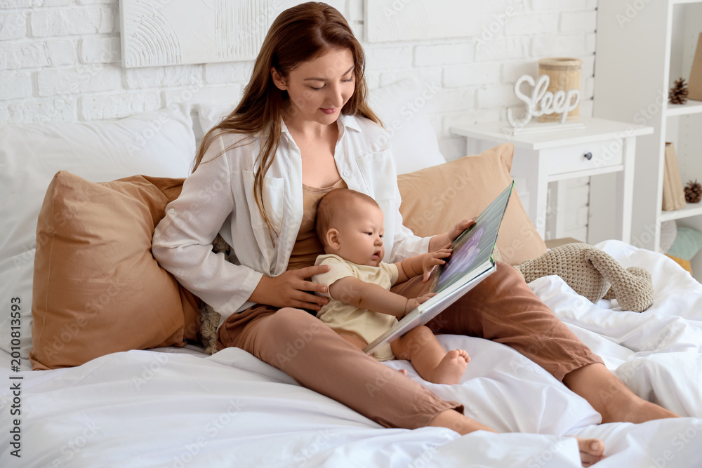 Fototapeta premium Mother with her baby reading book on bed at home