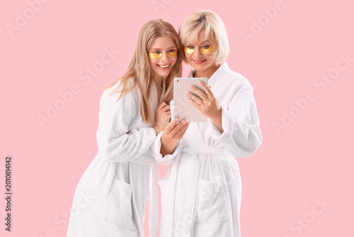 Happy young woman and her mother in bathrobes with under-eye patches holding ...