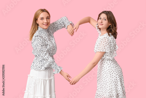 Beautiful mature woman with her daughter showing heart gesture on pink backgr...