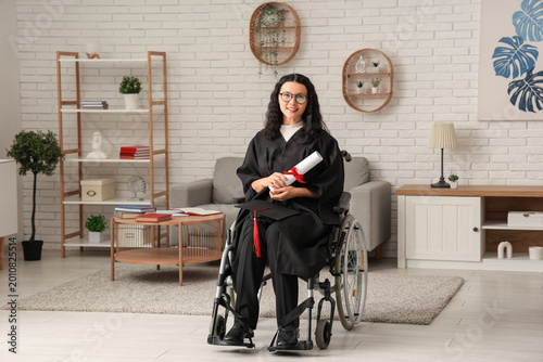 Beautiful female graduate student in wheelchair with graduation cap and diplo...