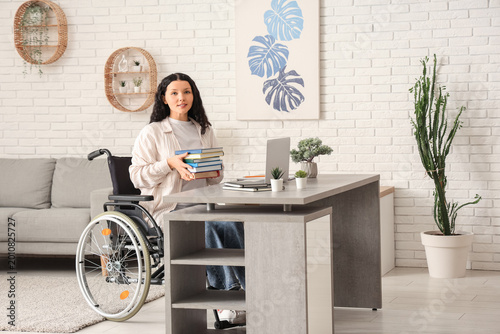 Beautiful female student in wheelchair with laptop and books studying online ...
