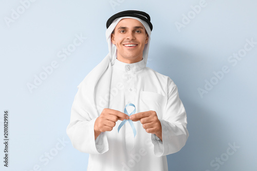Handsome Muslim man with blue ribbon on color background. Prostate cancer con...