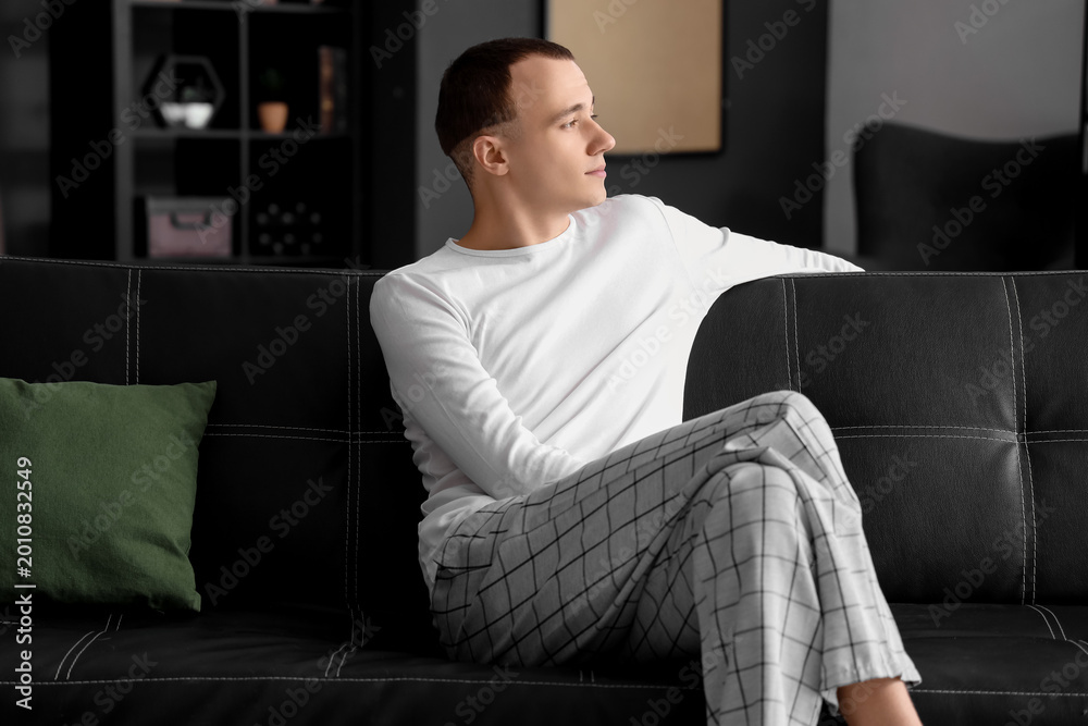 Fototapeta premium Young man sitting on black couch at home