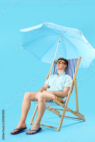 Young man resting in deck chair on blue background