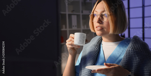Female nurse with cup of coffee working evening shift in clinic, closeup
