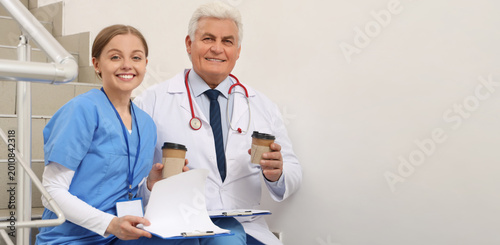 Mature doctor and nurse with coffee sitting on stairs in clinic