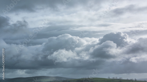Dramatic low angle shot of massive cumulus clouds forming an imposing stormy sky with deep gray hues and soft white edges against a muted green horizon for atmospheric weather photography
