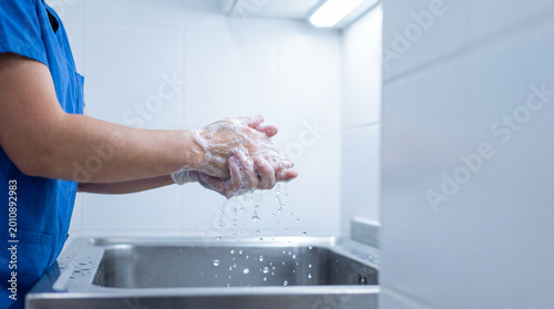 Healthcare worker washing hands with soap over stainless sink in clinical room emphasizing hygiene protocol infection prevention patient safety sanitation procedure nursing practice medical compliance