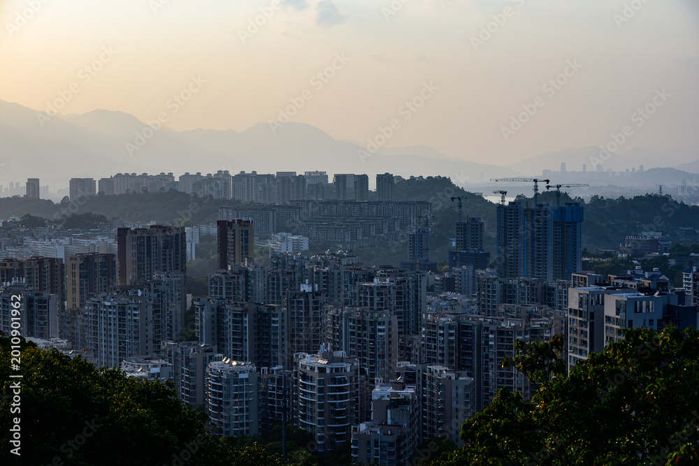 Fototapeta premium Distant sunset scenery in Fuzhou. The sun slowly sets behind Tianshan Mountain, overlooking the Minjiang River. Riverside city buildings line the bank, blending mountain, river and urban architecture.