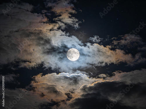 Majestic full moon emerging through dramatic swirling clouds illuminated by soft ethereal light casting a serene celestial glow against a deep twilight sky with intricate fluffy textures