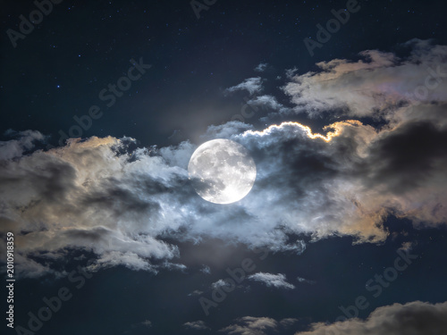 Majestic full moon glowing through dramatic night clouds creating a serene celestial atmosphere with soft silver illumination contrasting against deep navy sky and fluffy cumulus formations