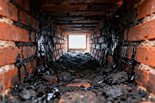 Vertical Interior View of a Chimney Flue with Thick Glossy Black Creosote Tar Deposits Choking the Passage
