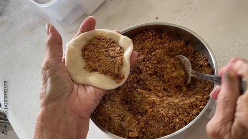 A close-up shot captures the process of using a spoon to add a generous amount of sweet ground peanut filling into a circular dough wrapper for handmade baozi.