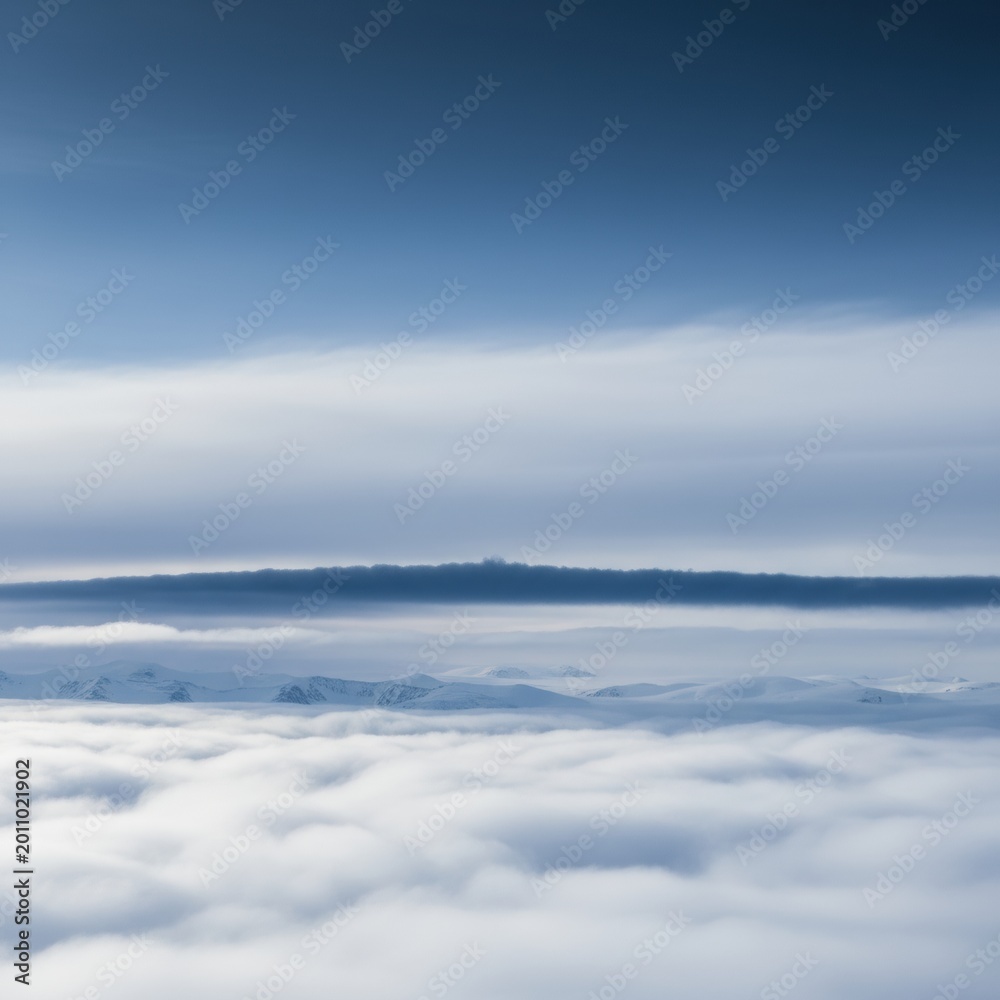 Naklejka premium White clouds and blue sky filling the frame over distant snowy mountain peaks for travel background, airline advertising and winter nature website styling