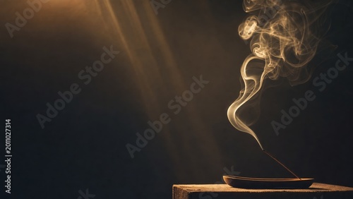 Incense stick burning with smoke rising in dramatic dark light