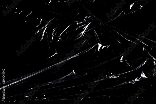 Foto Transparent plastic wrap texture with wrinkles and glossy reflections on black background
