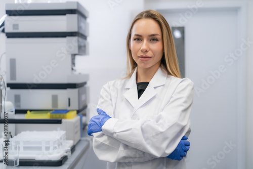 Laboratory technician standing confidently with arms crossed in a modern clinical research setting.