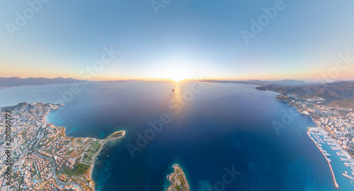 Foto Kusadasi, Turkey - July 4, 2025: Aerial panorama of bay with Pigeon Island, yacht marina, and cruise liner sailing away in sun glimmer at sunset