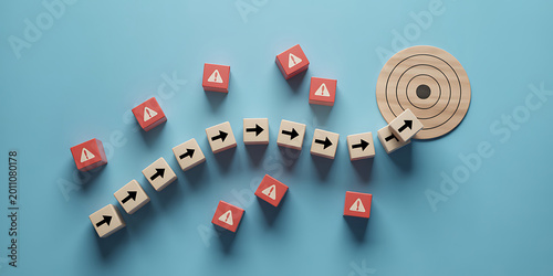 Wooden blocks with arrows and warning signs on a blue background forming a curved path to a target