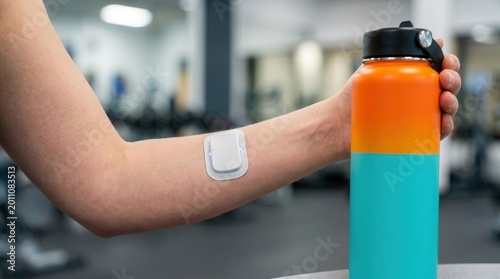 Person Wearing a Continuous Glucose Monitor (CGM) Sensor on Arm Holding a Water Bottle in the Gym