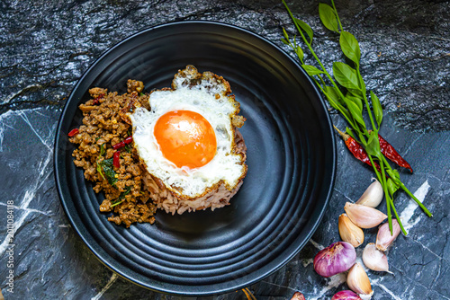 Stir fried minced pork with basil steamed rice fried egg spicy Thai food garlic chili herb Asian cuisine delicious meal top view black plate marble background lunch dinner homemade traditional