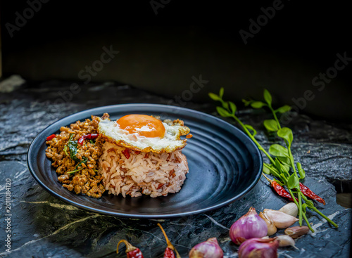 Stir fried minced pork with basil steamed rice fried egg chili garlic shallot Thai food spicy savory Asian cuisine black plate rustic background