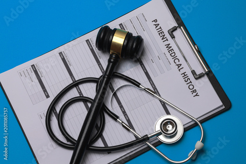 Serious legal gavel and stethoscope on patient medical history clipboard showing ethical concern about medicine and malpractice justice