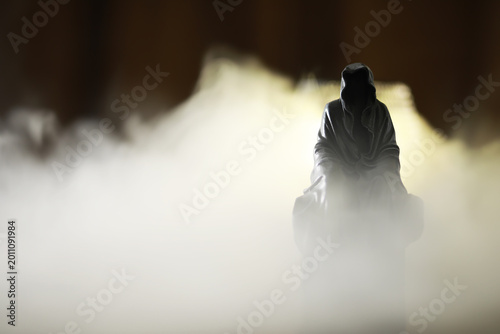 Fotografie Mystical hooded figure surrounded by ethereal fog in a dark, mysterious setting