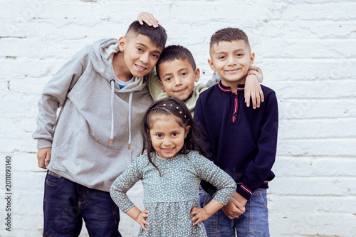 Four latin american children smiling and posing together against white brick wall