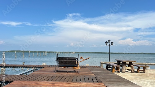 bay, beach, beautiful, blue, bridge, cloud, coast, day, dock, Wooden terrace with a swing chair and wooden table set overlooking the calm sea and traditional fishing stake