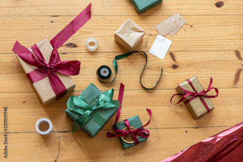 Cluster of wrapped gifts sitting on wooden tabletop with ribbons, tags, tape, twine