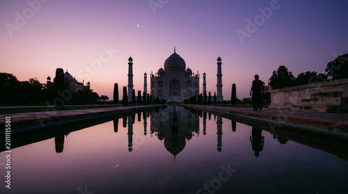 The Taj Mahal stands majestically against a serene purple and pink sunset background reflected in water