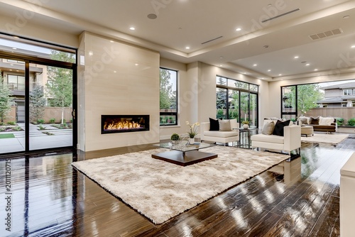 Living room offers an open floor plan with a clean fireplace feature, polished hardwood floors, and large sliding doors that lead out to a well-manicured garden area during the daytime hours.