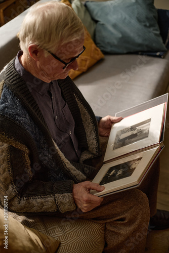 Foto Senior Caucasian man sitting and viewing family photo album, reflecting on personal memories and life history