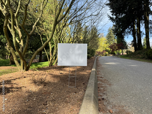 Yard sign mockup near the walking path in the park. Blank yard sign in green grass on sunny day